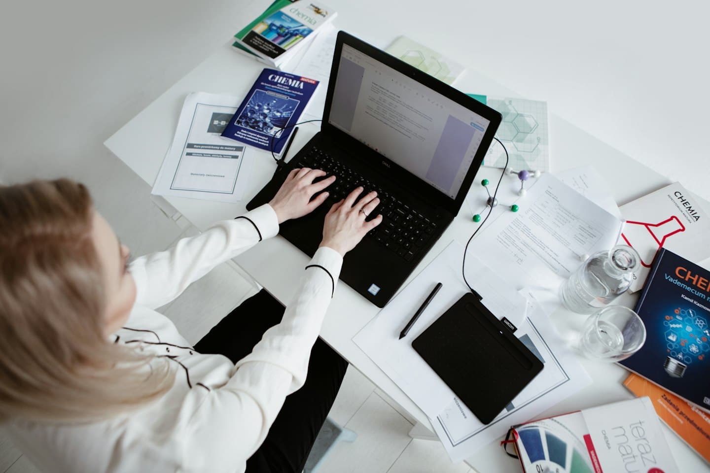 Una donna digita su un laptop a una scrivania con libri di testo di scienze.