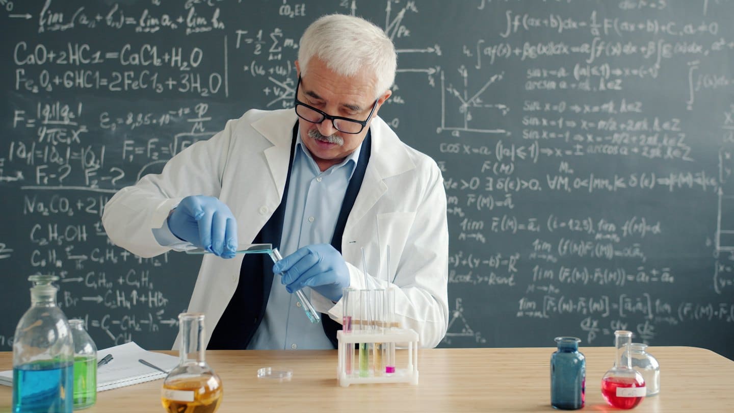 Scienziato versa liquido blu tra provette su un tavolo da laboratorio.